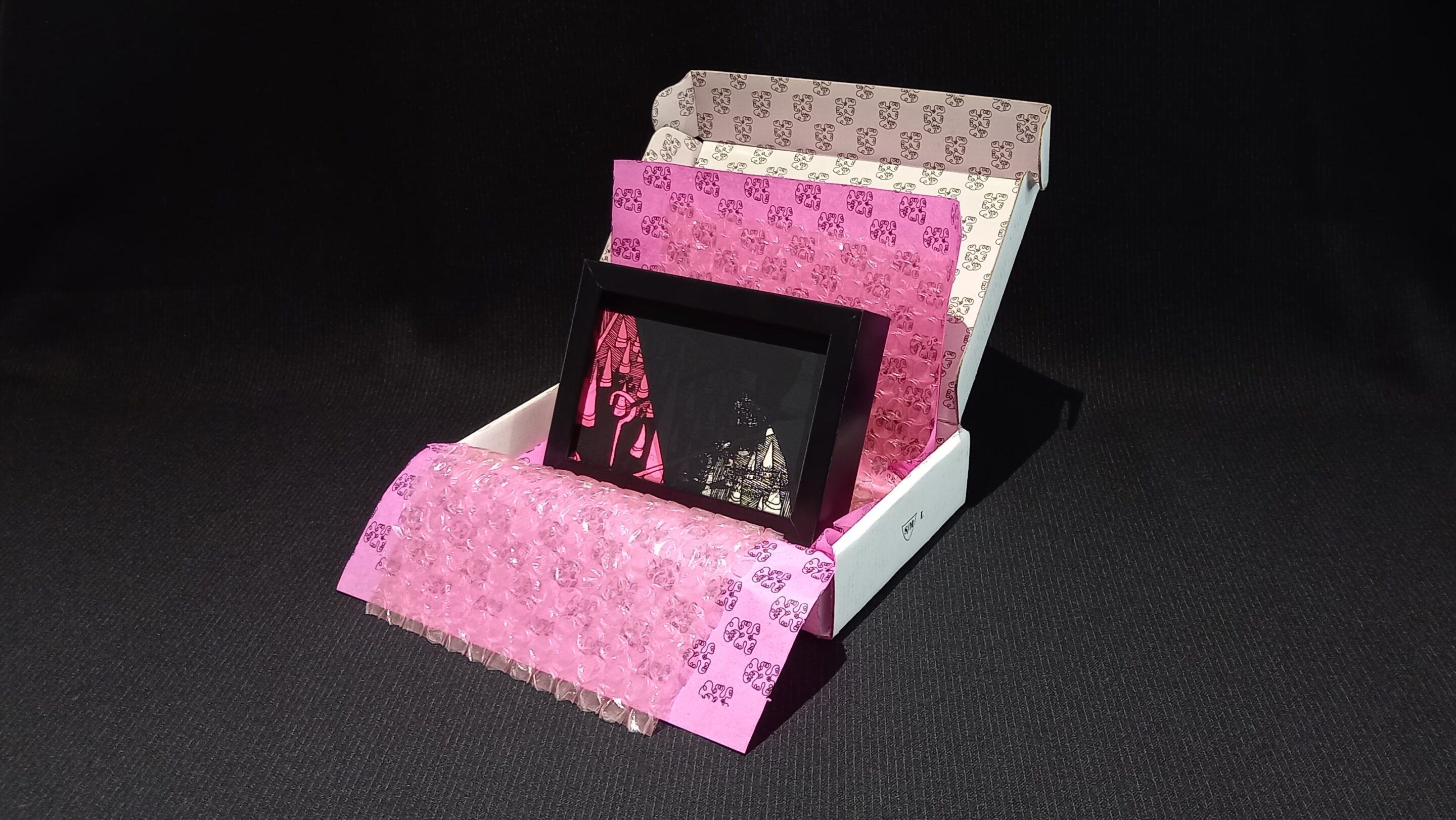 Œuvre encadrée en noir et blanc, sérigraphie unique avec parfois des rehauts de peinture fuchsia. Emballage soigné : papier bulle, papier de soie, et boîte en carton double cannelure décorée à la main en sérigraphie.